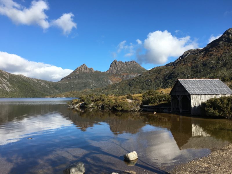 The mirror-like surface of the lake at Cradle Mountain with the iconic boathouse and mountain peaks in the distance.