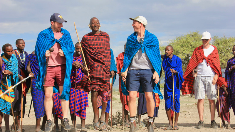 Two travellers jumping with Maasai warriors