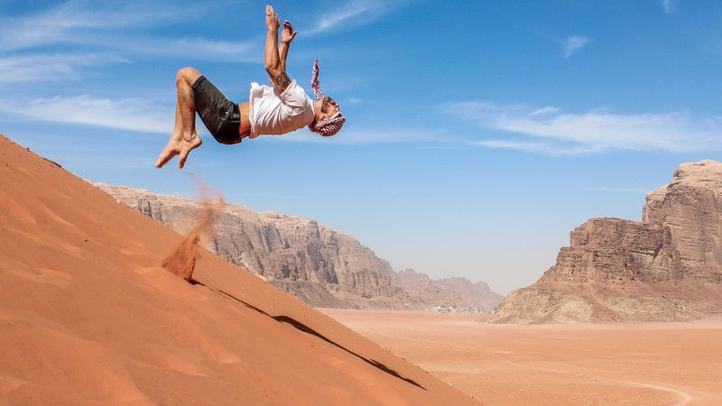 A man backflips off a sand dune