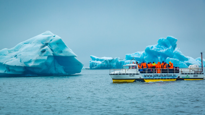 A group of travellers viewing giant, bright blue icebergs from a yellow boat.