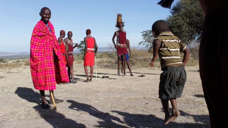 a young boy jumping as high as he can next to a group of men performing the jumping ceremony on a Kenya safari