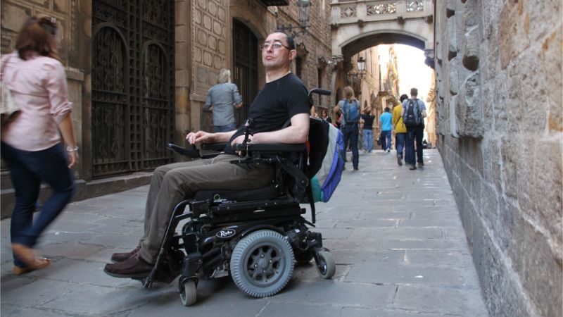 A man in a wheelchair in a cobbled lane in Spain