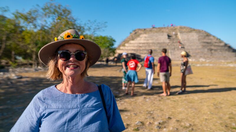 A woman wearing a hat smiles in front of a temple in Mexico