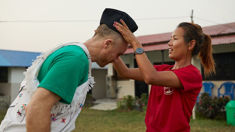 A woman puts a hat on a man in Nepal.