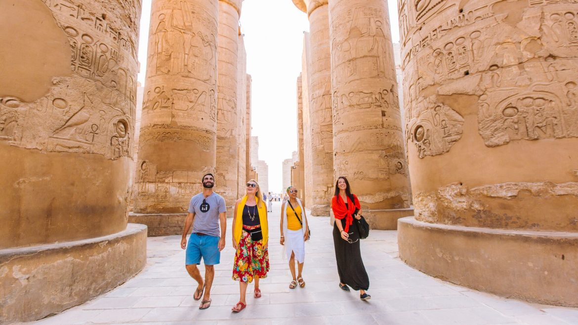 Four travellers walking between huge temple pillars in Luxor, Egypt