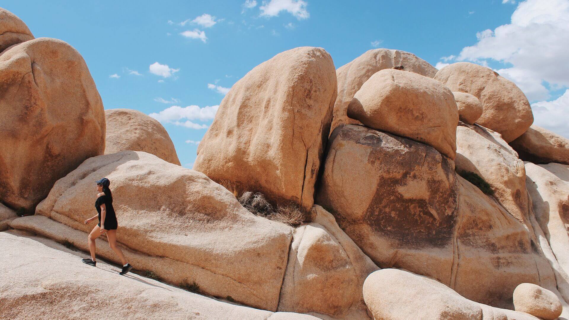 A hiker walks up a large rock formation in Joshua Tree National Park, Arizona, USA