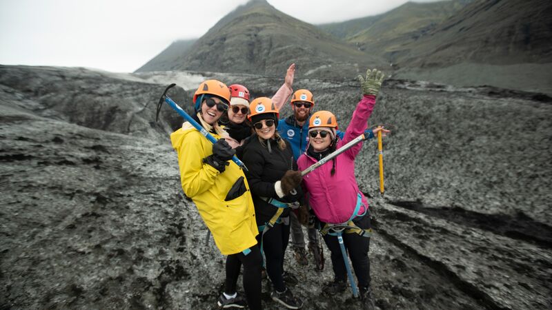 A group of travellers in brightly coloured jackets holding pick axes on a geyser in Iceland. 