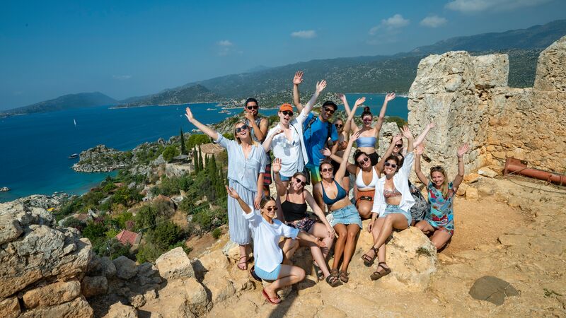 A group of travellers smiling at the camera at a lookout over the Turkish Coast. 