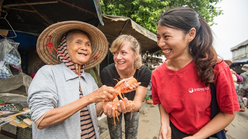 An Intrepid guide and traveller smile with a local woman wearing a large straw hat.