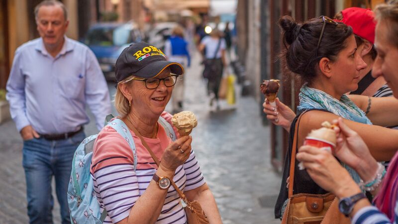 A traveller wearing a striped shirt and hat embroidered with "Rome" looks lovingly at a cone of gelato in her hand.
