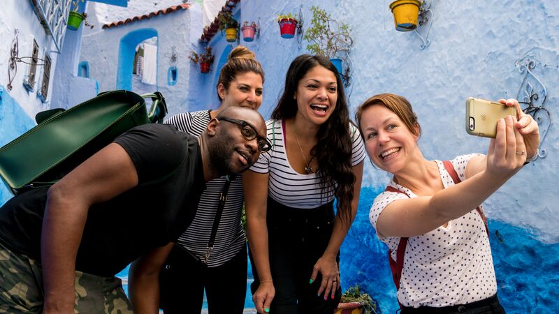 Four travellers pose for a selfie on a street where the walls are painted various shades of blue.