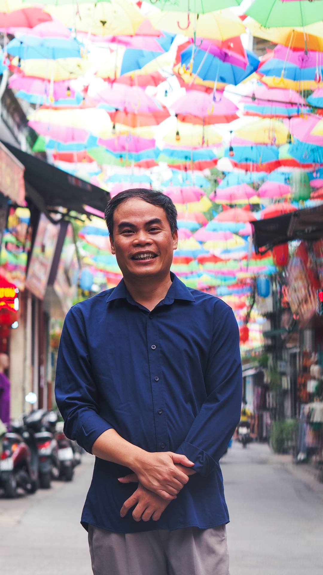 a man standing in a narrow street below hundreds of colourful umbrellas