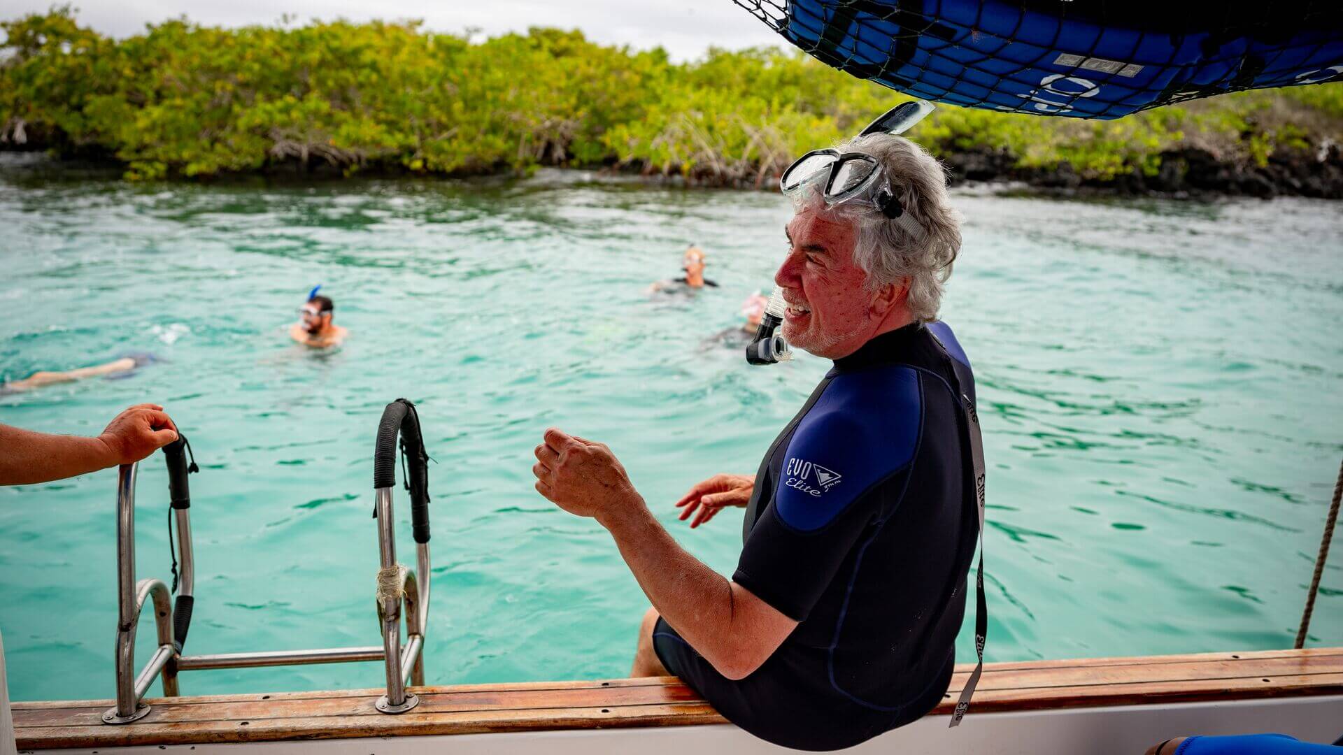 Man in wetsuit sitting on the edge of a boat while swimmers snorkel in the waters, Isla Isabela las Tintoreas