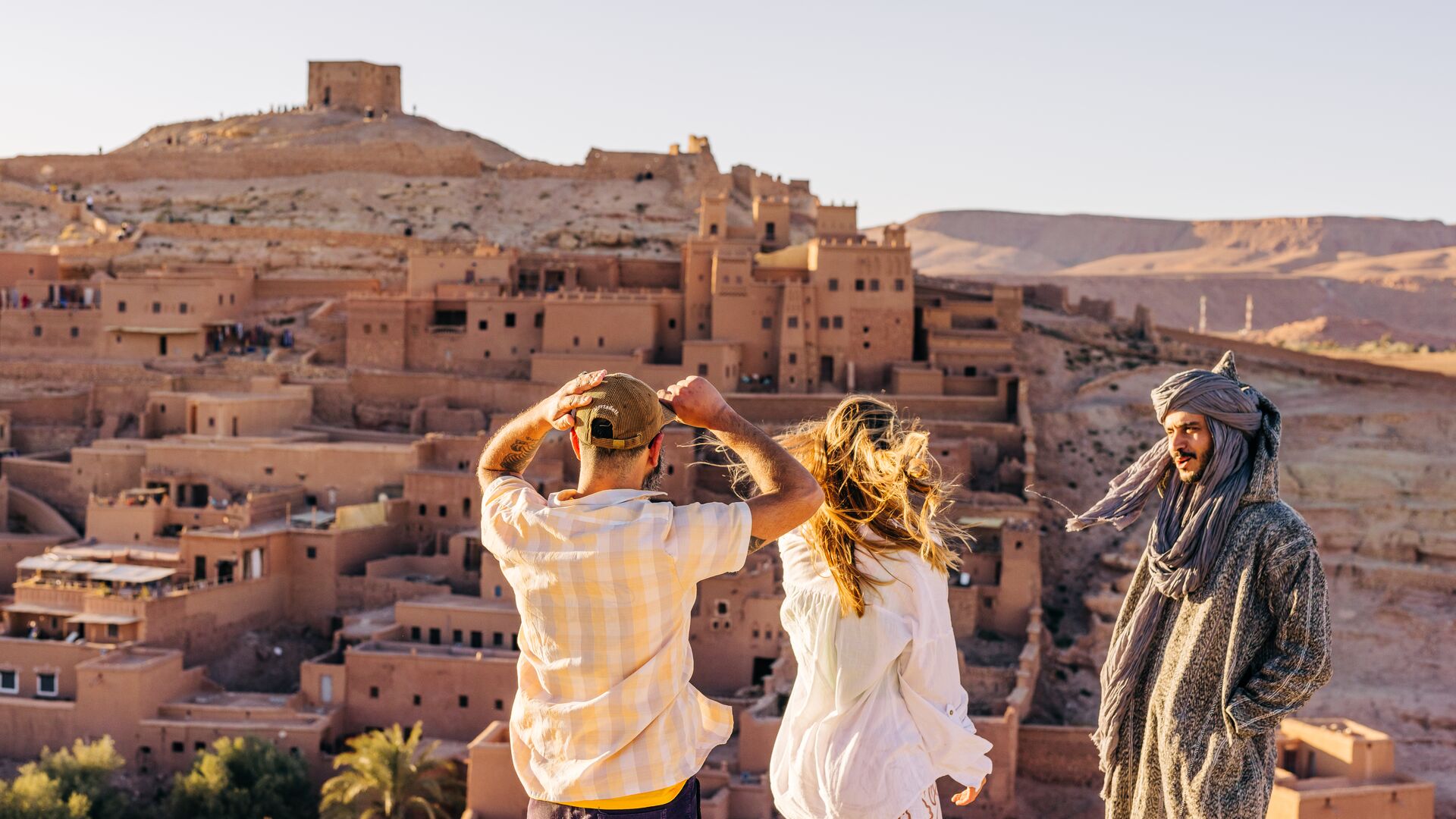 Two travellers and a local man looking at the historic city of Benhaddou, Morocco from a viewpoint