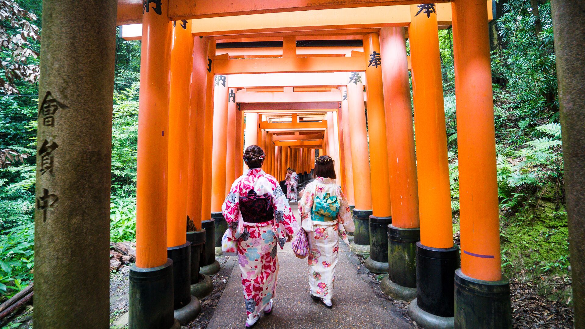 Two Japanese women strolling through Fushimi Inari Shrine in Kyoto wearing kimonos