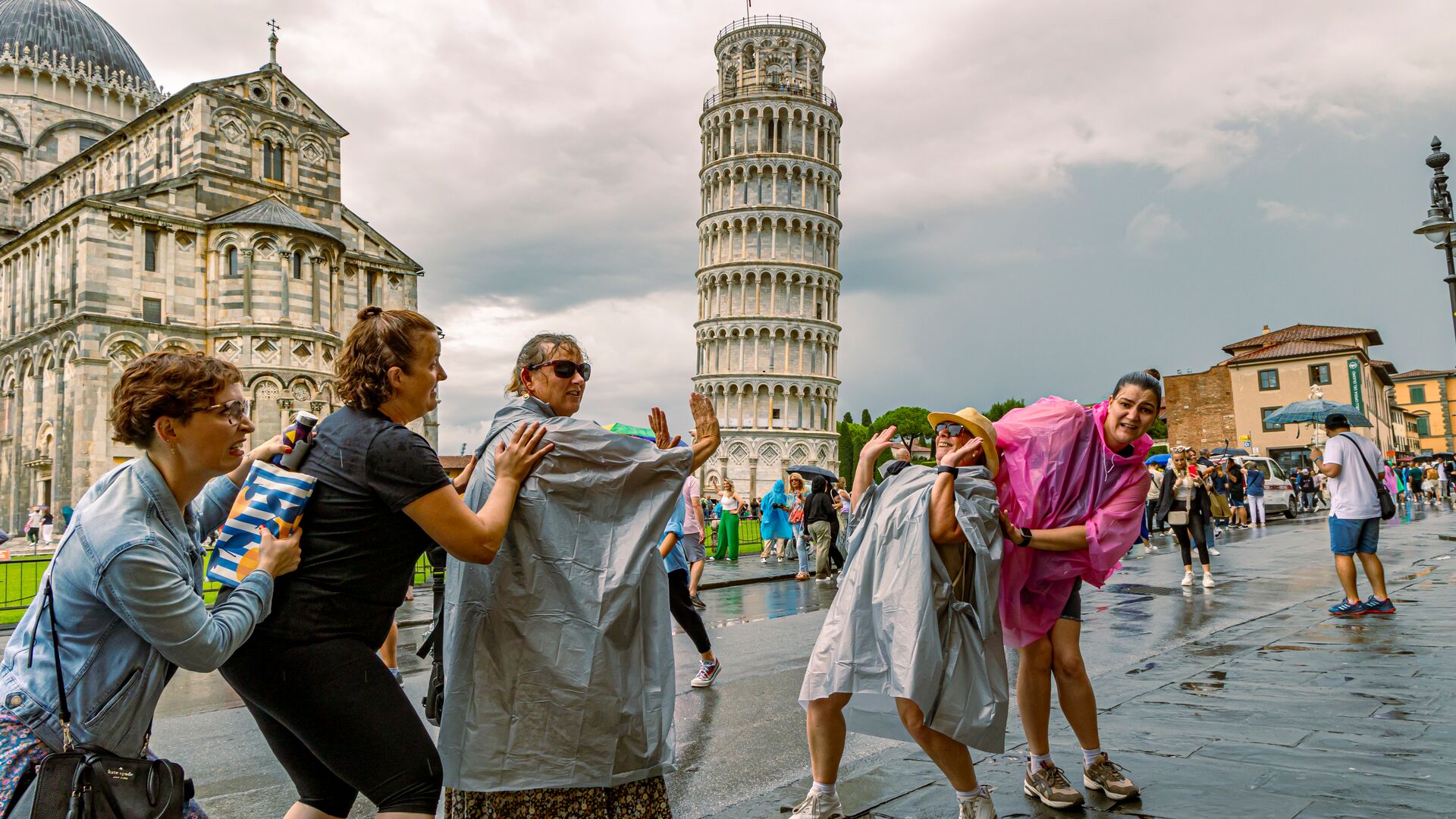 A group of five travellers taking silly photos with the Leaning Tower of Pisa in Italy