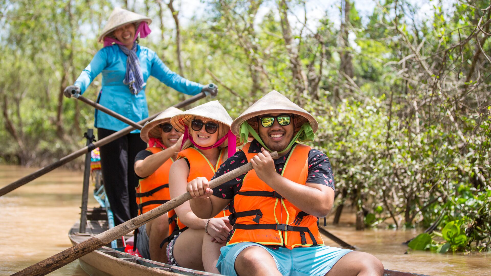 Three travellers riding in a traditional canoe with a local woman in Vietnam