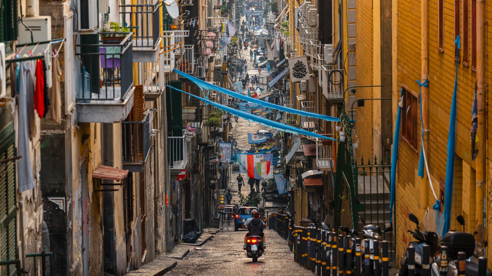 A scooter and car driving down a narrow street in the Old Town of Naples