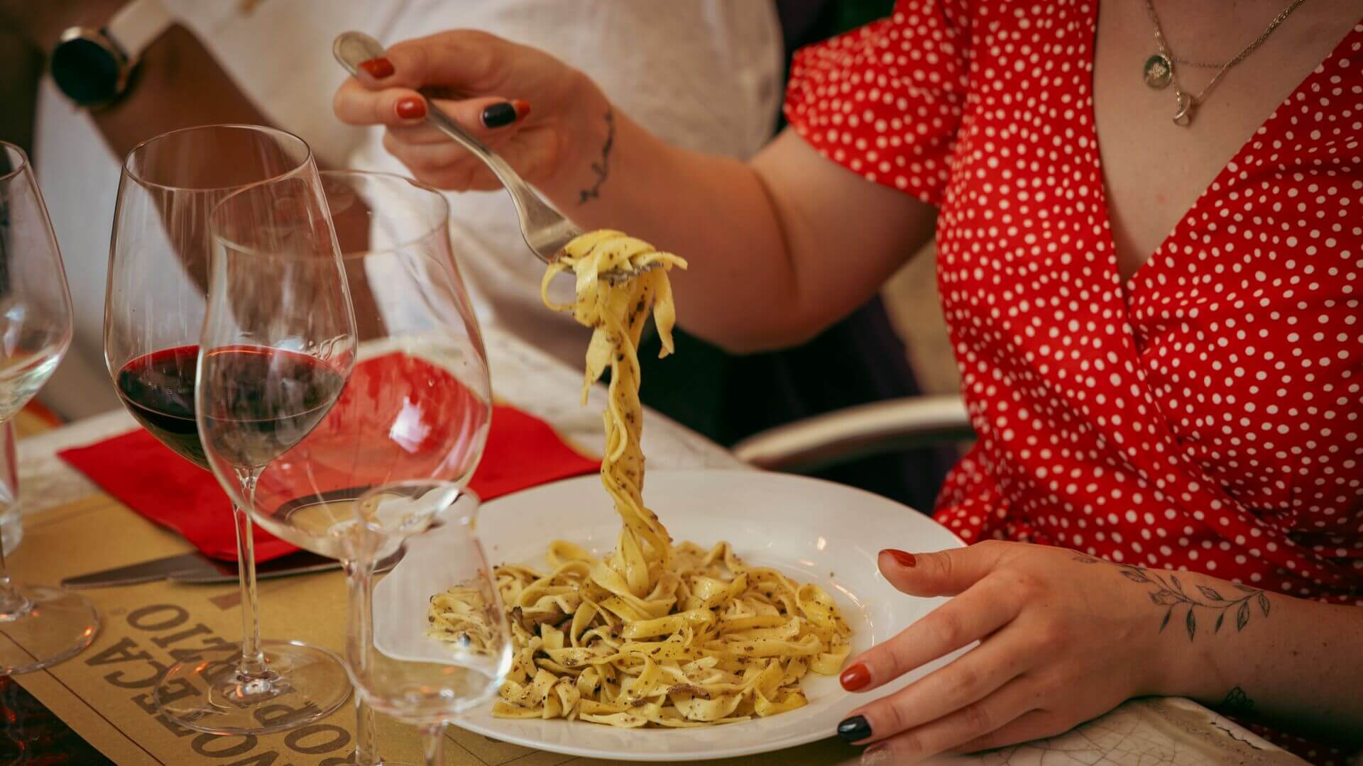 Person eating pasta and drinking red wine