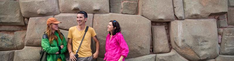A few travelers leaning against a stone wall in Cusco, Peru 