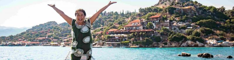 A traveler throws her arms up in glee while docked in the picturesque harbor of Kas