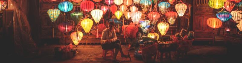 Local woman sitting in front of lit-up lanterns in Hoi An