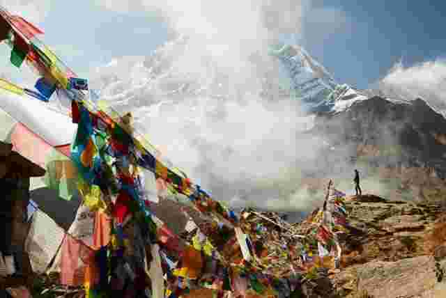 Traveller looking out over the scenery at Annapurna Basecamp with brightly coloured flags are in the foreground