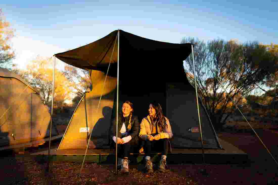 Two women travellers sitting out the front of a permanent tented camp in Australia's Red Centre 