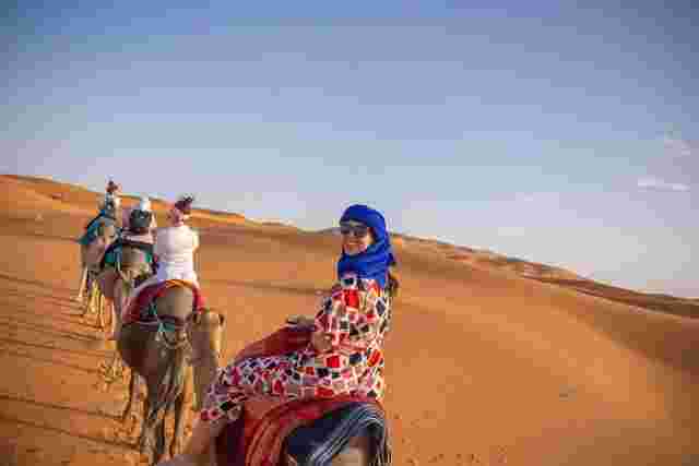 A traveler smiling as she rides a camel through the Sahara Desert in Morocco