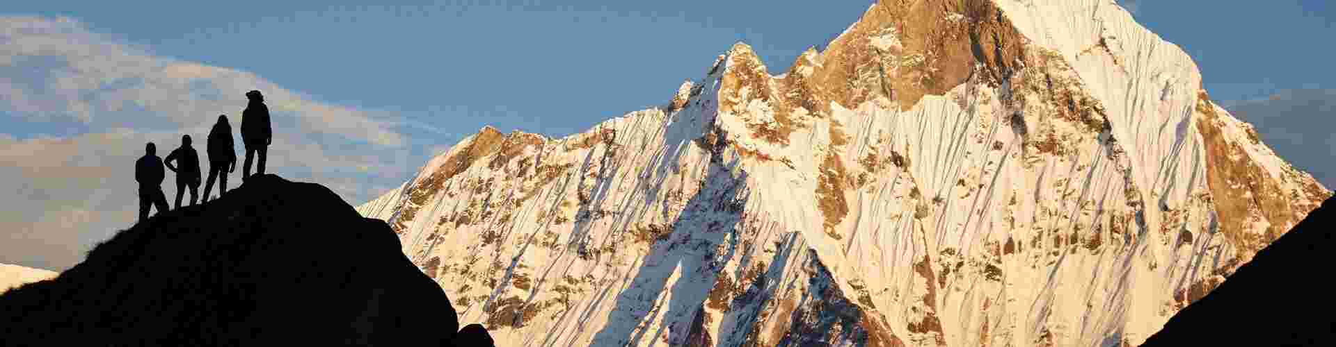 A group of hikers standing on a smaller peak at Annapurna basecamp in the shadow of a larger peak