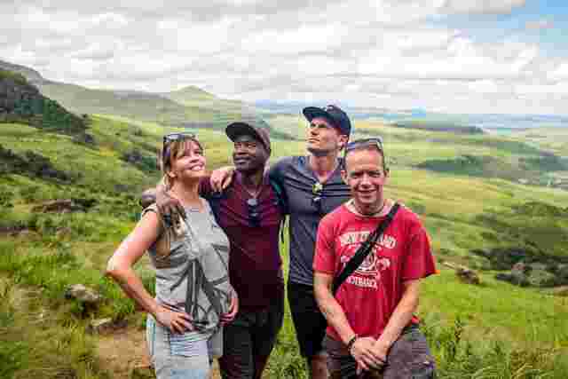 A group of travellers poses on a lush green mountainside while hiking the Drakensberg Mountains