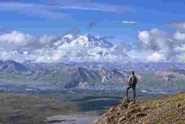 Travellers standing on a rocky peak overlooking the mountain range of Denali. 