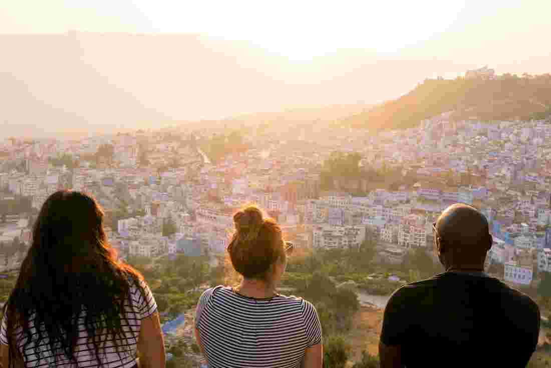 Three travellers sit on a high overlook looking out over blue painted buildings of Chefchaouen
