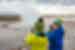 Young travellers smile and watch as Strokkur geyser erupts in front of them as they film on their phones