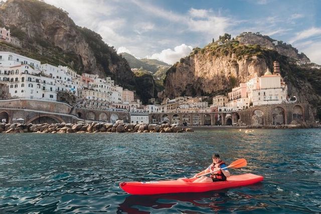 A traveller smiles as she kayaks along the Amalfi Coast with towering cliffs and colourful buildings